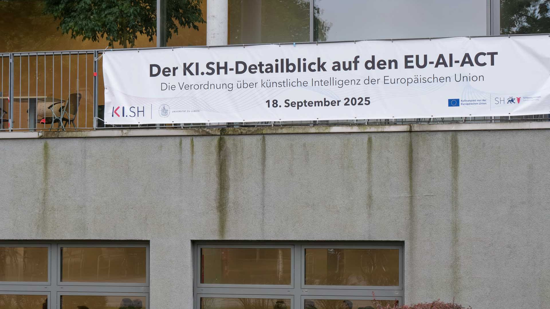 An einer Fassade hängt ein Banner, das die Veranstaltung bewirbt